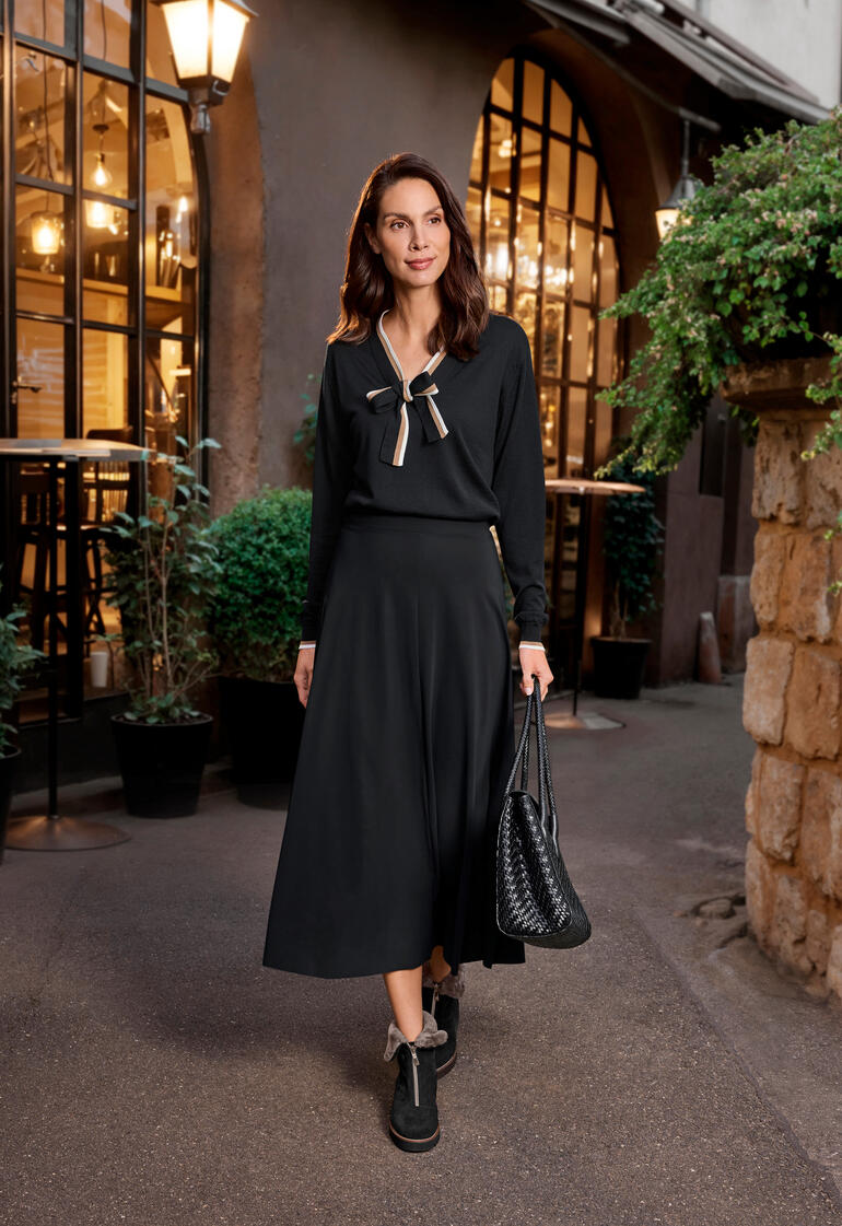 Frau in schwarzem Kleid mit zugband auf Gehweg vor einem Café