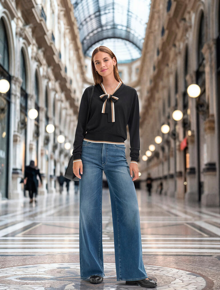 DL1961 Bequeme Jersey-Jeans Frau im eleganten Outfit mit schwarzem Bindeshirt und weit geschnittenen Jeans in einer Passage.