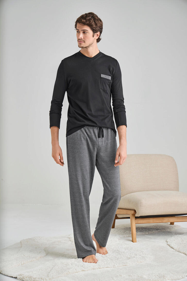 Mann in schwarzem Langarmshirt und grauen Pyjamahosen steht auf einem Teppich.