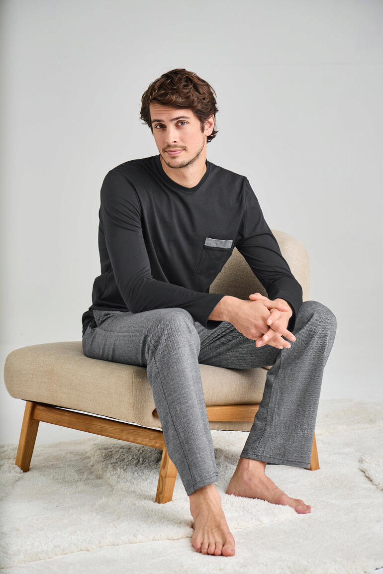 Lieblings-Pyjama lang Mann sitzt auf einem Sessel in schwarzem Langarmshirt und grauen Pyjamahosen.