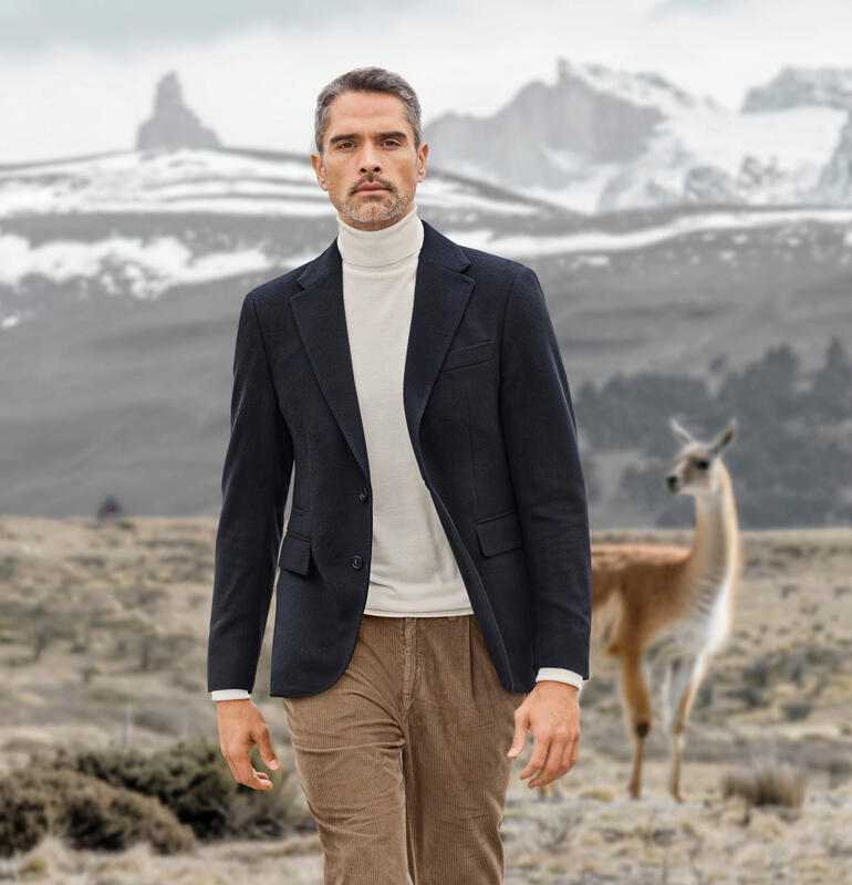 Vicuña-Blazer Vicuña-Blazer in Marineblau, Model geht durch Landschaft mit Lama im Hintergrund.