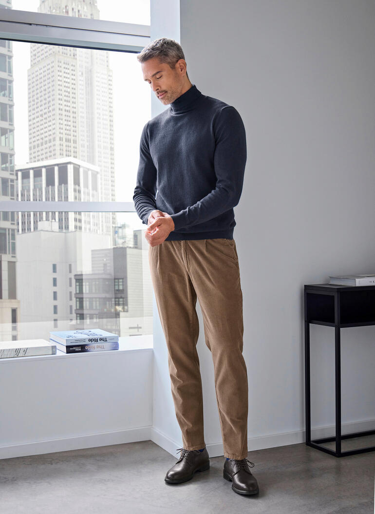 Ragman Feinstrick-Rolli in Dunkelblau, stehend am Fenster.