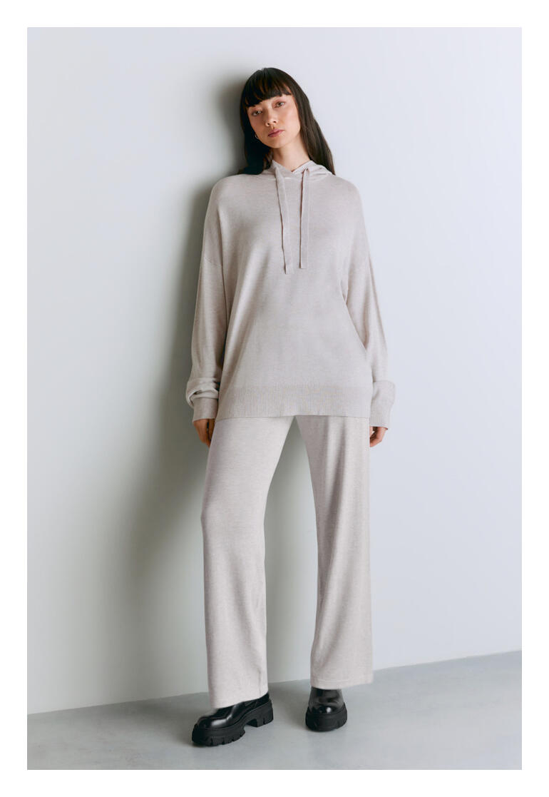 Lyocell/Kaschmir-Hoodie Frau in hellgrauem Lyocell/Kaschmir-Hoodie, steht vor einer Wand.