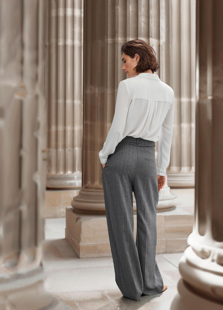 Frau von hinten in einem eleganten Outfit, zeigt die Nadelstreifenhose.