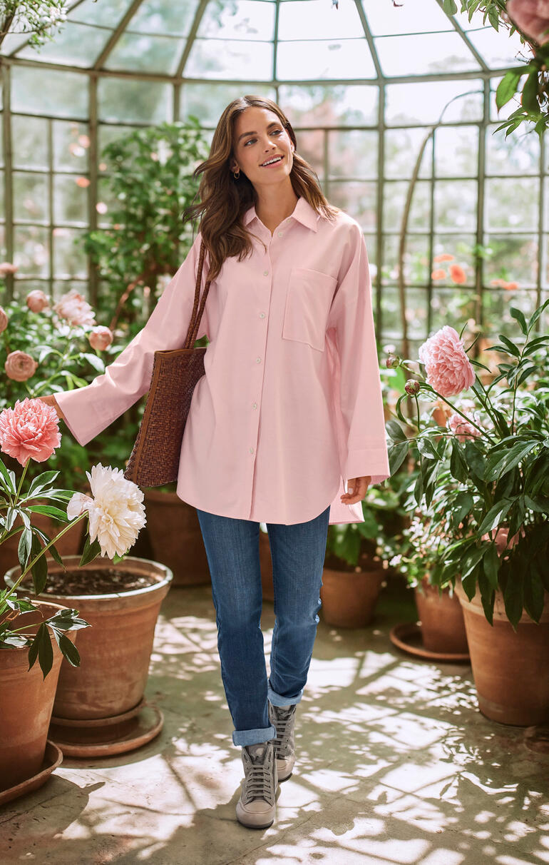 Oversize-Winterbluse Frau in einer rosa Oversize-Winterbluse steht in einem Gewächshaus.