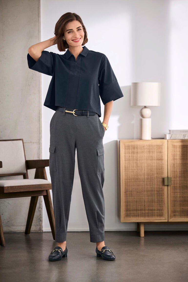 Navy Frau in einem Boxy Oversize-Blusenshirt, kombiniert mit eleganten Hosen, im modernen Interieur.