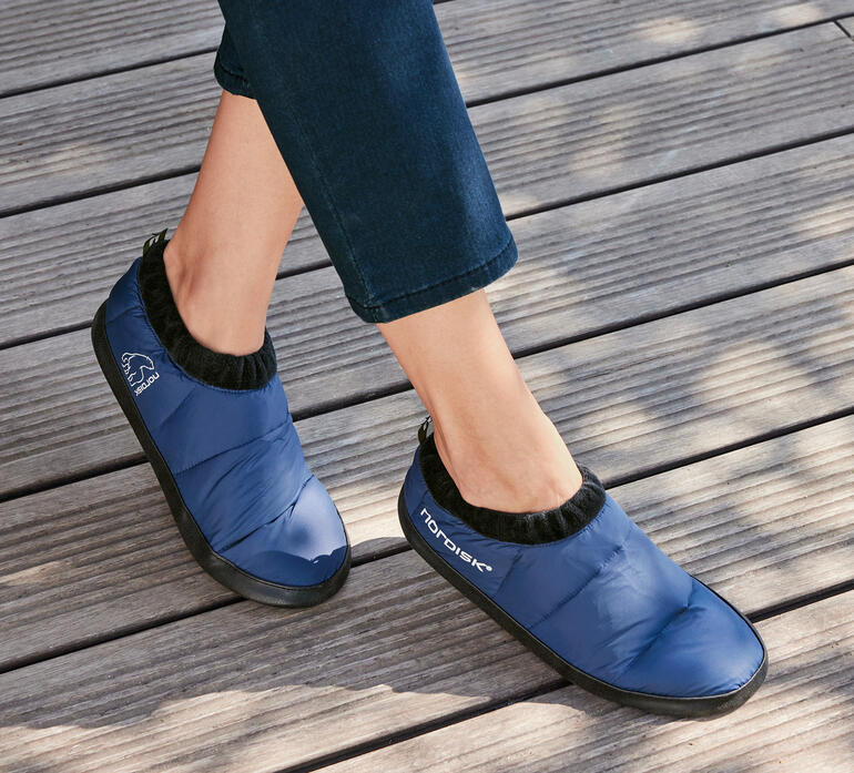 Dunkelblauer Nordisk Daunenschuh, getragen von einer Person auf Holzboden.