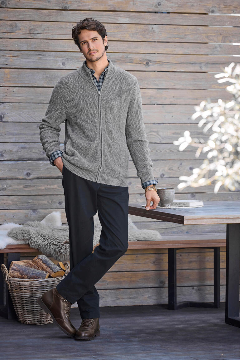 Grau Mann in einer grauen Alpaka-Klima-Strickjacke vor einer Holzwand