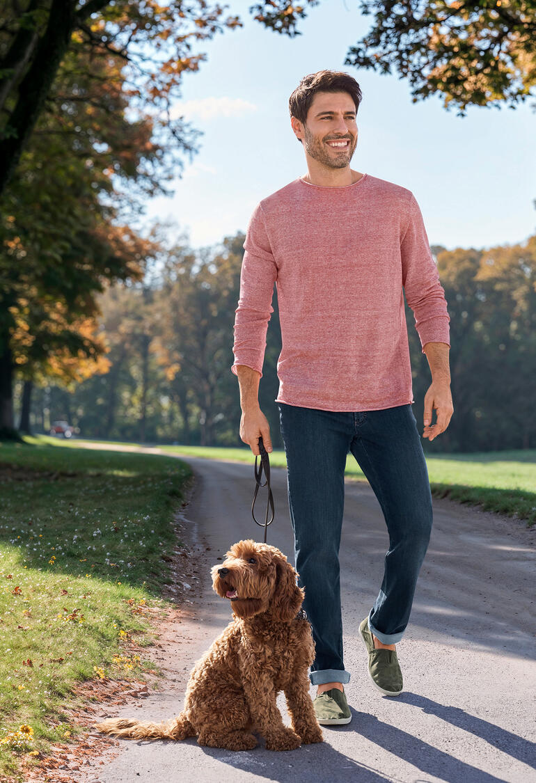 Mann in einem rosanen, leichten Pullover, geht mit einem Hund auf einem Weg.