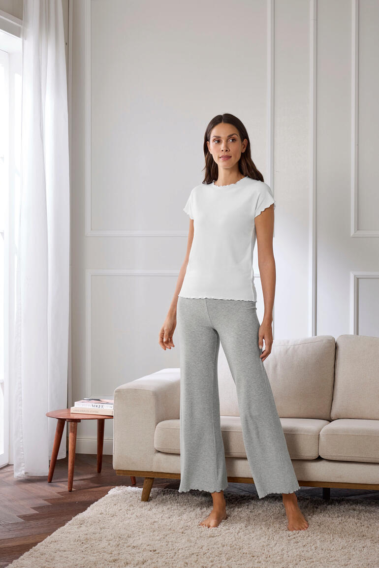 Shirt und Hose Frau steht in grauem Modal-Rippstrick-Pyjama und weißem T-Shirt vor einer Couch