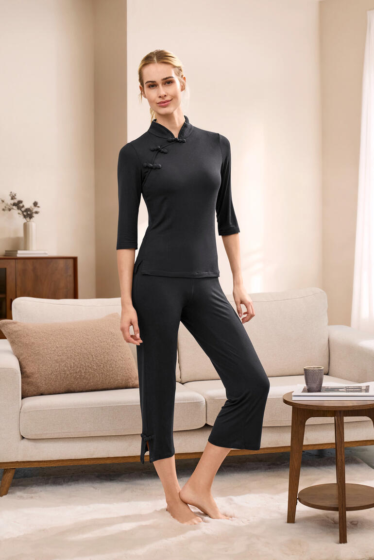 Frau in schwarzem Dreamsack-Pyjama mit langem Arm steht in einem Wohnzimmer.