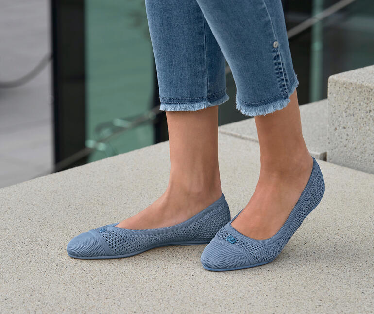 Bleu Frau trägt blaue Mesh-Ballerinas, steht im Freien auf Steinboden.