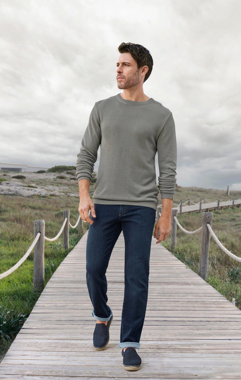 Espadrij l’originale Sommer-Slipper Mann in einem grauen Ivanhoe Tencel-Piqué-Pullover und Jeans auf einem Holzsteg.
