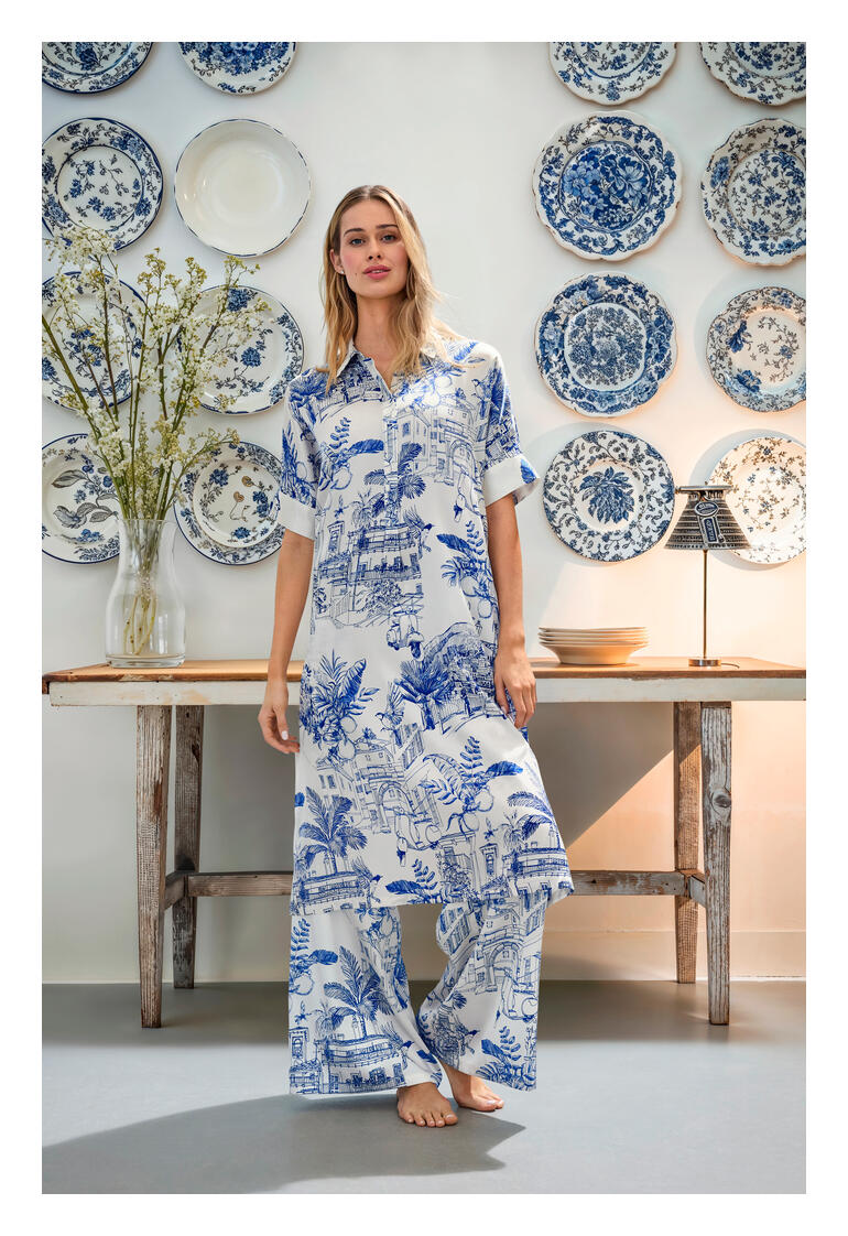 Blusenkleid und Wide-leg-Hose Frau in Esisto Seidenstretch-Kombination steht vor blauen Teller-Wänden.