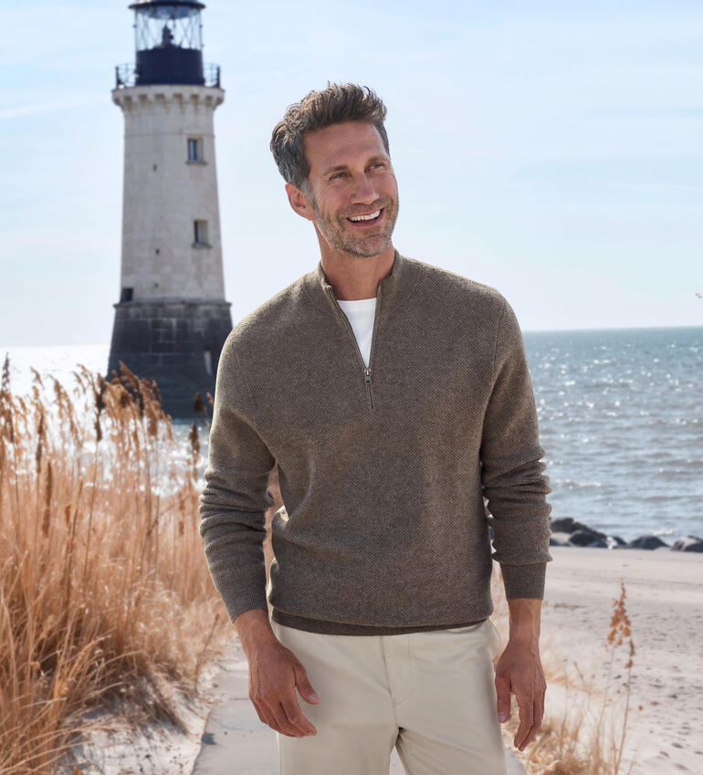Mann trägt einen Pullover an einem Leuchtturm am Meer