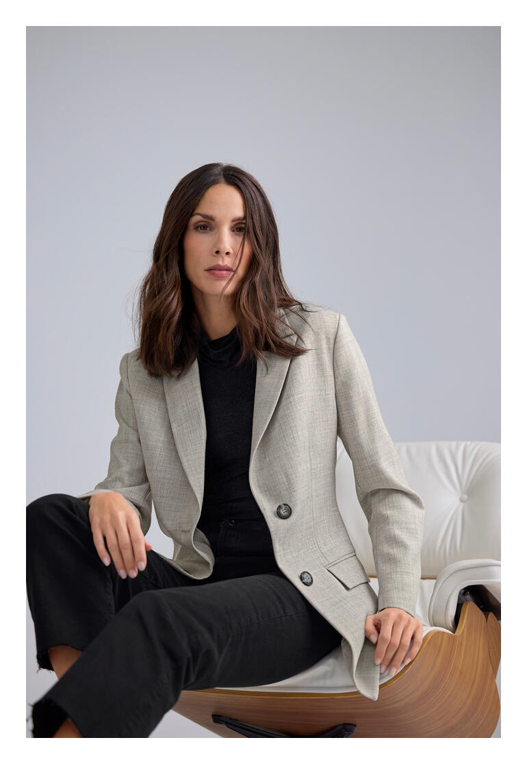 Frau sitzt in einem Sessel und trägt einen grauen Blazer.