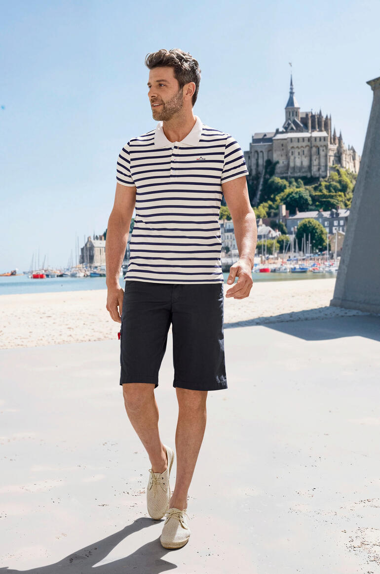Mann in gestreiftem Saint James Bretagne-Poloshirt beim Spazieren am Strand.