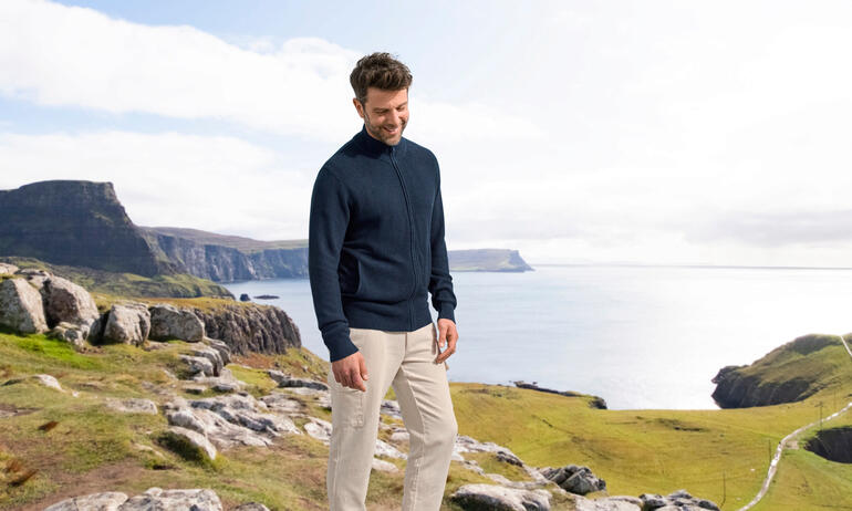 Seiden-Klima-Cardigan Mann trägt einen navyfarbenen Seiden-Klima-Cardigan, stehend vor einer Küstenlandschaft.