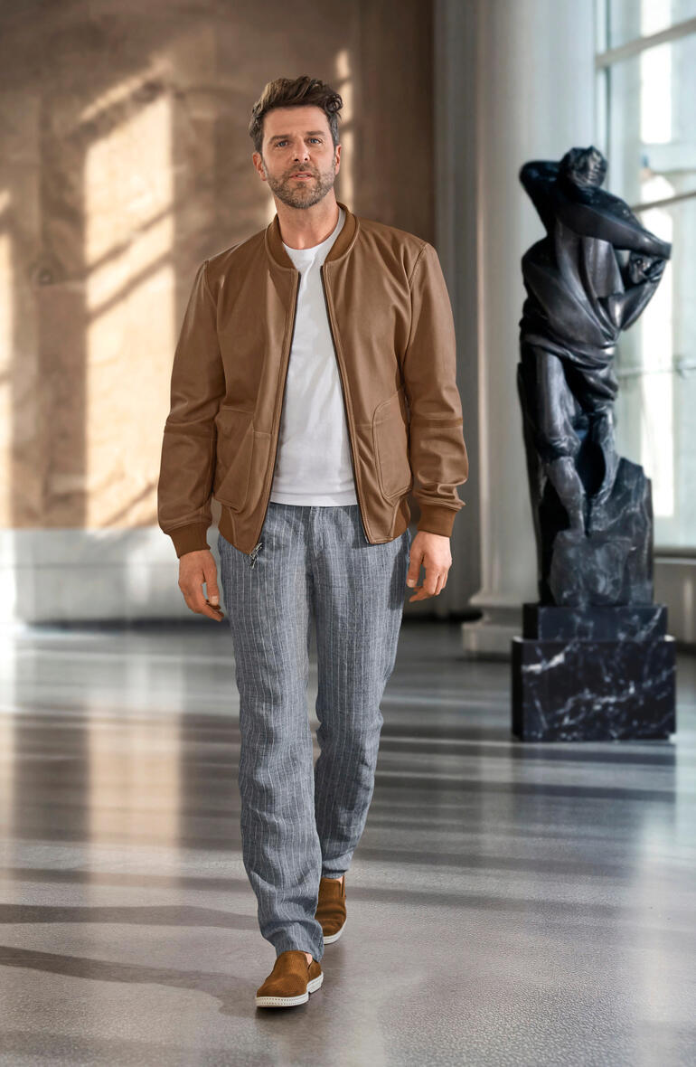 Mann trägt einen braunen OCONI Metis-Wendeblouson, mit Statue im Hintergrund.