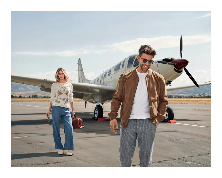 Zwei Personen in modischer Kleidung stehen vor einem Flugzeug.