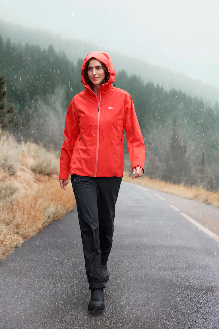 Dame in roter Hardshell-Jacke auf nasser Straße in einer bewaldeten Umgebung.