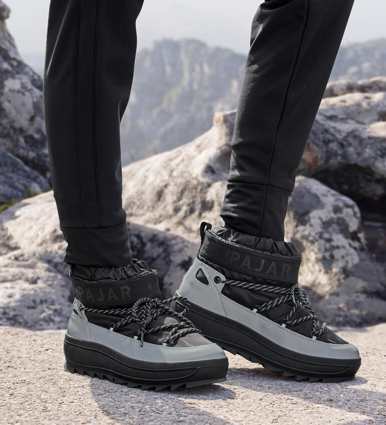 Frau trägt silberne Reflektor-Boots von Pajar in einer gebirgigen Landschaft.