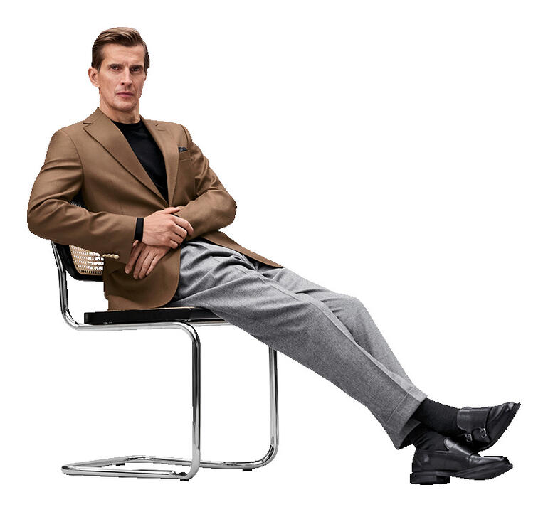 Carl Gross Hopsack-Blazer Mann sitzt in braunem Blazer auf einem Stuhl mit lässiger Pose.