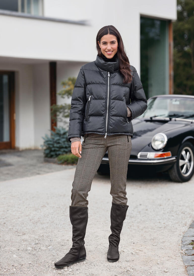 Frau in schwarzer Daunenjacke steht vor einem Auto auf einem Weg.