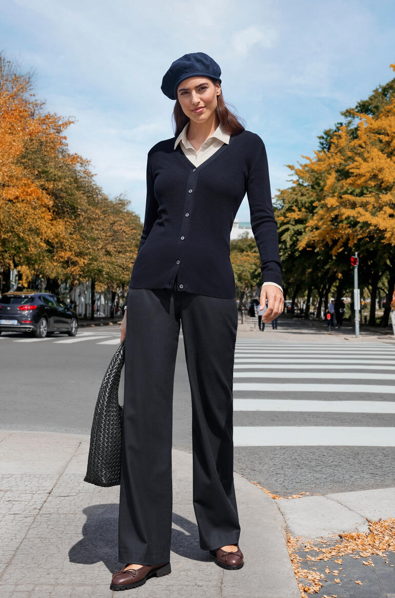 Frau in dunkelblauer Strickjacke und schwarzer Hose in herbstlicher Umgebung.