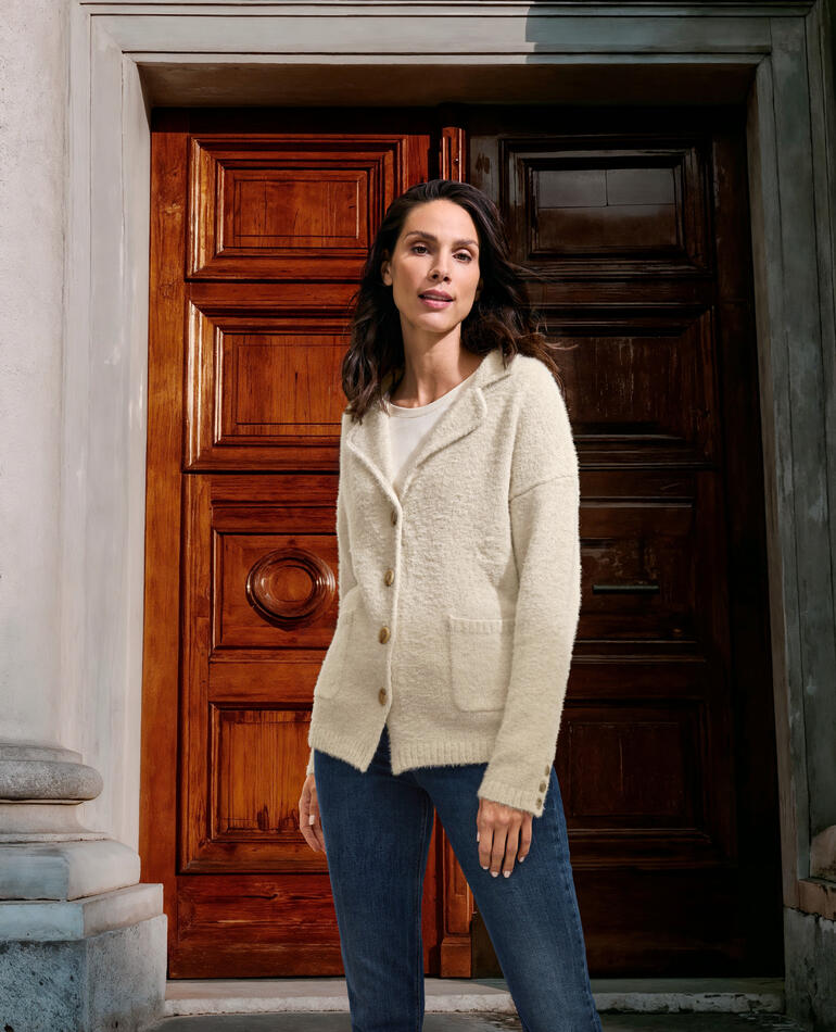Flausch-Strickblazer Frau in ecrufarbenem Strickblazer steht vor einer historischen Tür.