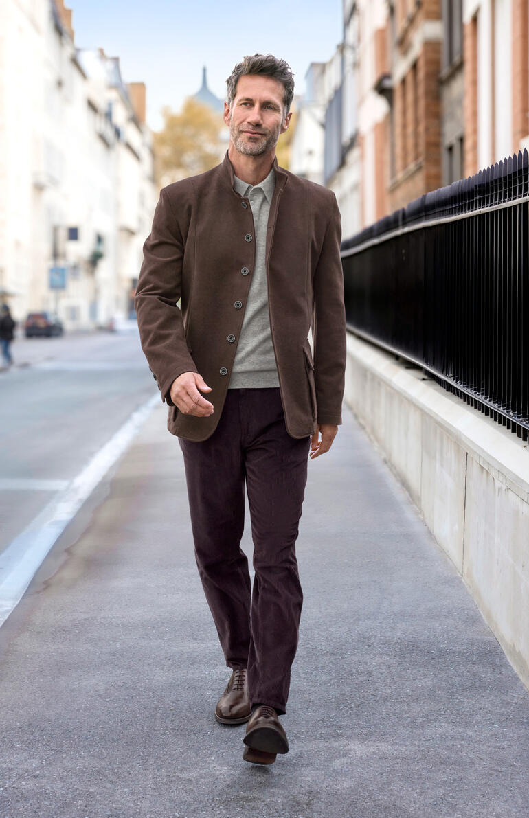 Weintraube Mann in einem braunen Moleskin-Jacket geht in einer urbanen Umgebung