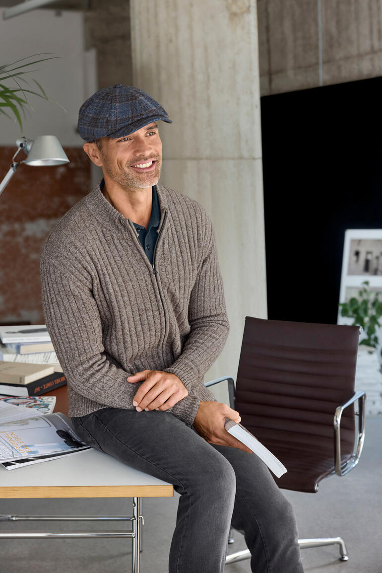 Mann in grauem Pullover mit Papierhut, lächelnd am Tisch sitzend, Größe 56