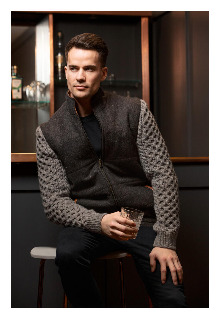 Mann trägt eine braun-graue Celtic-Tweed-Jacke, sitzt mit einem Glas.