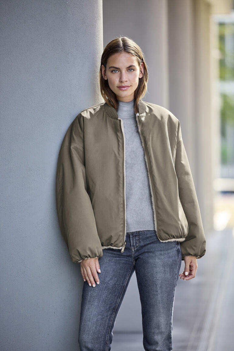 Studio AR Bomber-Wendejacke in neutralen Farben, Model steht lässig an einer Wand.