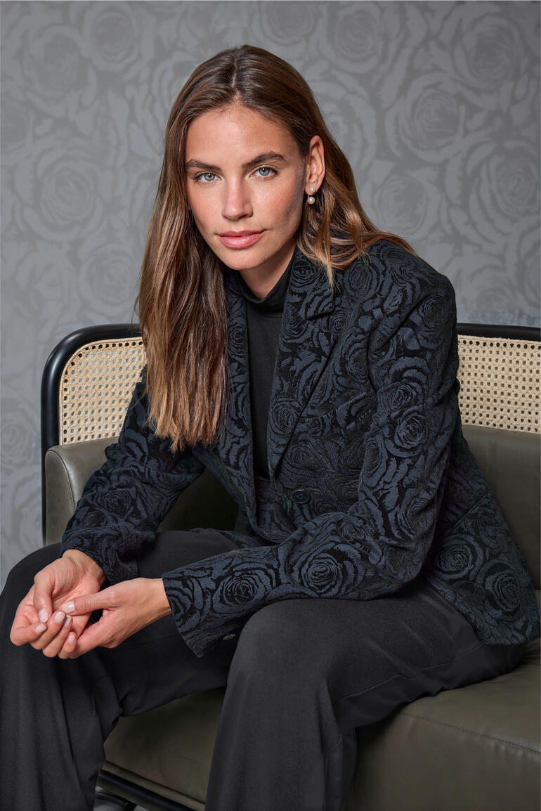 Rosen-Flanell-Blazer Frau in floral-gesticktem Blazer sitzt in stilvollem Raum.