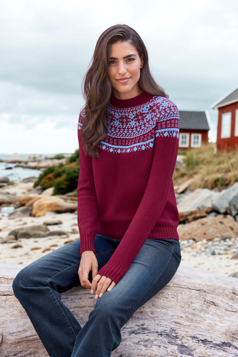 Frau in rotem Fair-Isle-Pullover mit blauem Muster an Küste.