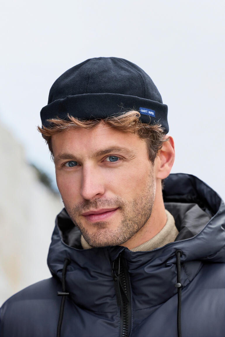 Mann mit Mütze in Winterjacke, lächelt vor unscharfem Hintergrund.