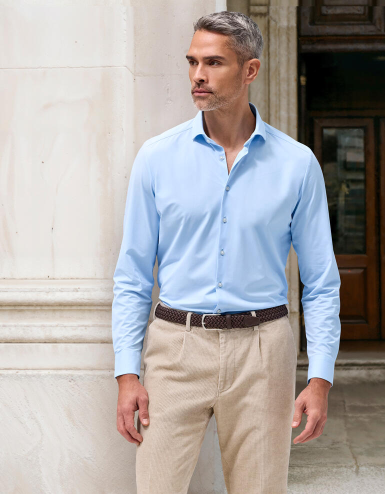 Mann in hellblauem 24-Stunden-Hemd, Größe 38, vor steinernem Hintergrund.