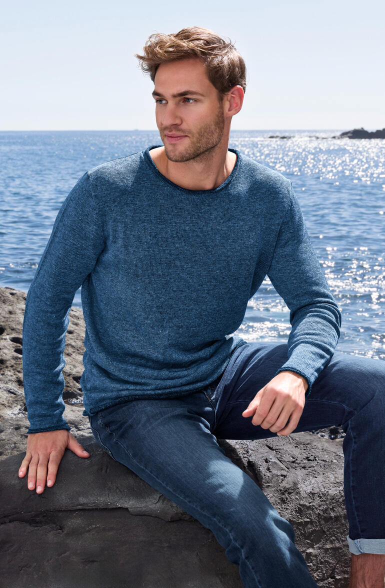 Mann trägt blauen Doubleface-Pullover, Blick auf Küstenlandschaft.