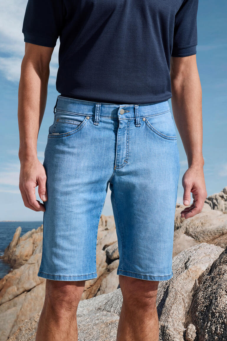 Mann in hellen Jeans-Shorts auf Felsen in maritimer Umgebung