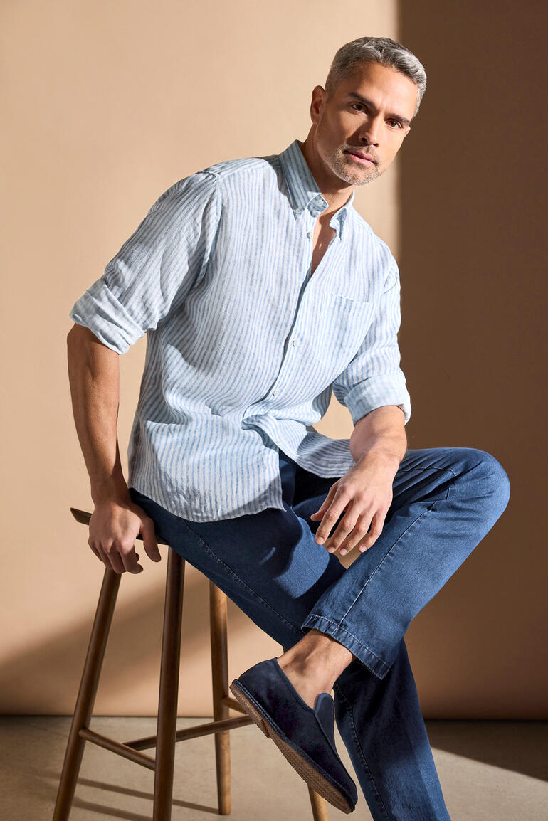 Mann in gestreiftem Lyocell-Leinenhemd in Weiß-Blau, Größe 38, auf einem Hocker sitzend.
