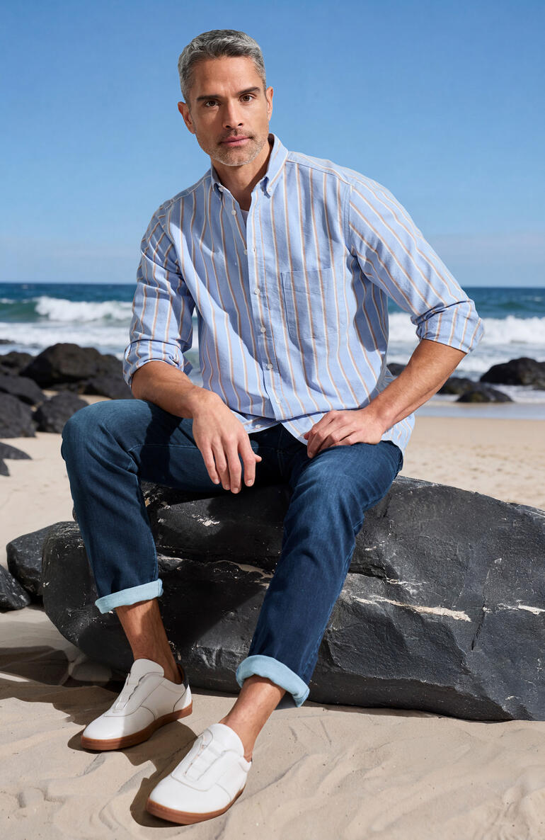 Mann trägt ein kariertes Hemd am Strand mit Felsen.