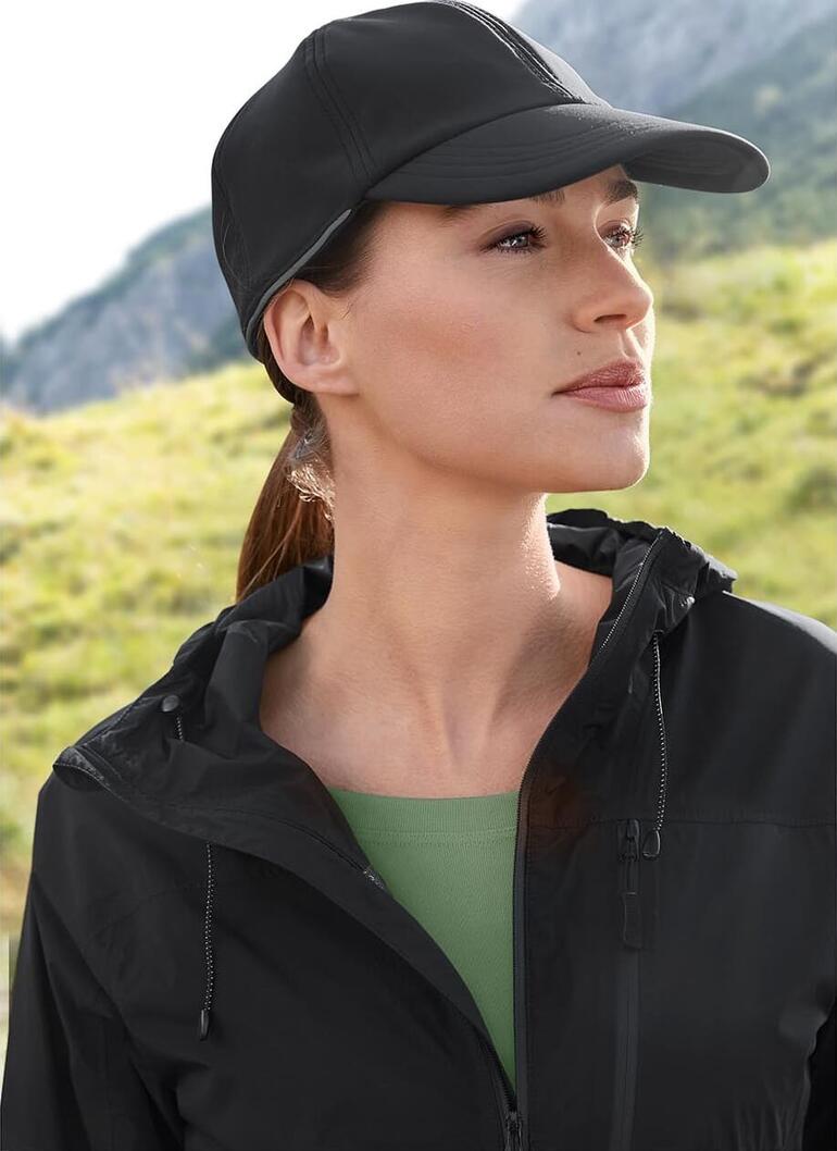 Softshell-Kappe Frau mit schwarzer Softshell-Kappe und Jacke in einer Naturlandschaft.