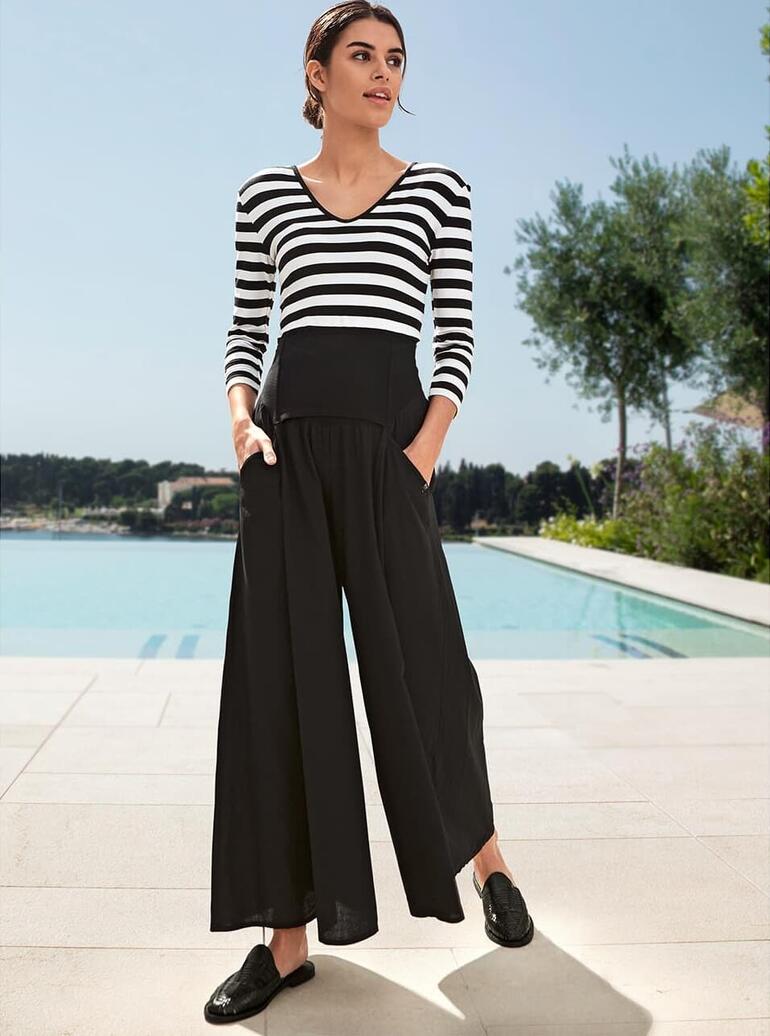 Elisa F. Ibiza-Hosenrock Frau in gestreiftem Zauber-Shirt mit schwarzer Hose, steht vor Schwimmbad.
