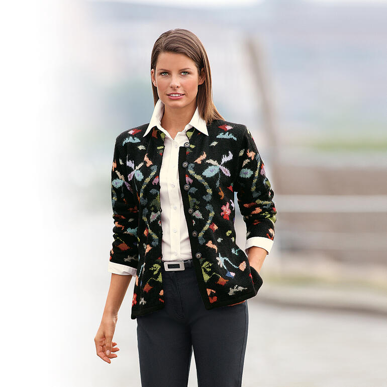 Schwarz/Multicolor Alpaka Cardigan Flowers, getragen von einer Frau vor unscharfem Hintergrund.