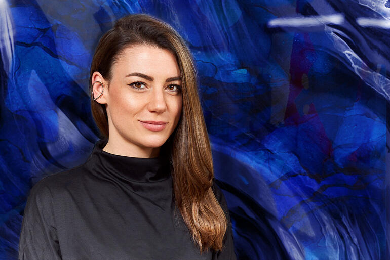 Porträt von Michèle Caspers vor einem blauen, abstrakten Hintergrund.