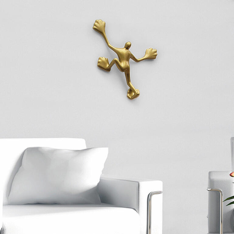 Flossi befestigen Sie einfach an Ihrer Haus- oder Wohnzimmerwand. Goldfarbener Wandhaken in Form eines Menschen, montiert an einer weißen Wand.