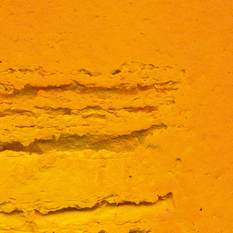 Die „Schrifttafel“ beeindruckt durch ihre lineare Struktur und enorme dreidimensionale Wirkung. Nahaufnahme einer strukturierten, orangefarbenen Oberfläche.