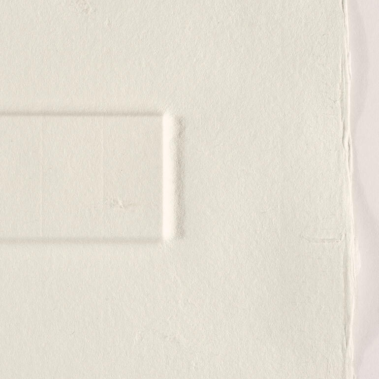 Das 300 g schwere Büttenpapier wird durch eine Druckplatte aus Legosteinen geprägt. Detailaufnahme einer strukturierten, hellen Fläche ohne Farbe
