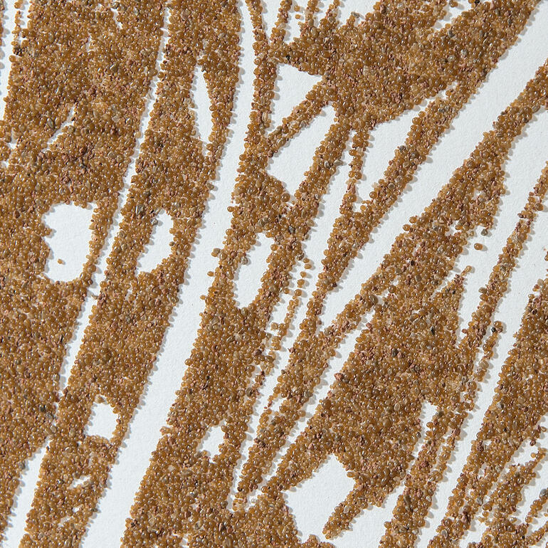 Der Künstler verwendet echten Wüstensand für seine Terragrafien.
Es lässt sich nicht vermeiden und ist vom Künstler angedacht, dass sich Sandkörner lösen können und am Boden des Rahmens ablagern. Detailaufnahme des strukturierten Papiers mit Sand für Günther Ueckers Kunstwerk.